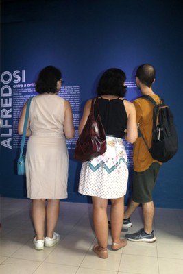 Público lendo texto de apresentação da exposição Alfredo Bosi: entre a Crítica e a Utopia
